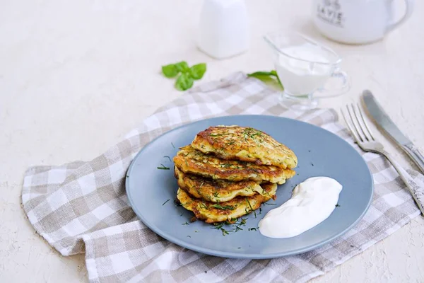 Fritters zucchini with feta cheese on a gray plate on a light concrete background. Served with sour cream. Zucchini recipes. Selective focus.