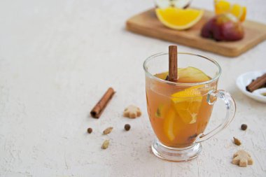 Baharatlı elma şarabı. Alkolik ya da alkolsüz taze filtresiz elma suyundan yapılmış baharatlar, elma dilimleri ve portakallı hafif beton bir arka planda cam bardak. Boşluğu kopyala.