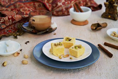 Fıstıklı Hint tatlıları, badem ve kakule beyaz bir tabakta açık beton arka planda. Masala çayıyla servis edilmiş. Geleneksel Hint tatlıları.