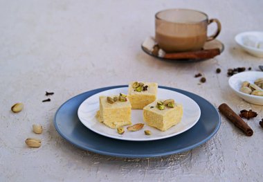 Fıstıklı Hint tatlıları, badem ve kakule beyaz bir tabakta açık beton arka planda. Masala çayıyla servis edilmiş. Geleneksel Hint tatlıları. Boşluğu kopyala.