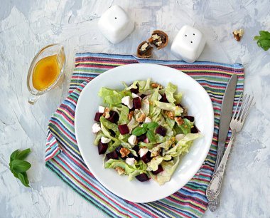 Haşlanmış pancar, feta ve fındıklı yeşil salata gri beton arka planda beyaz bir tabakta. Zeytinyağı, tahıllı hardal ve sirkeyle tatlandırılmış. Sağlıklı yiyecekler. Üst görünüm.