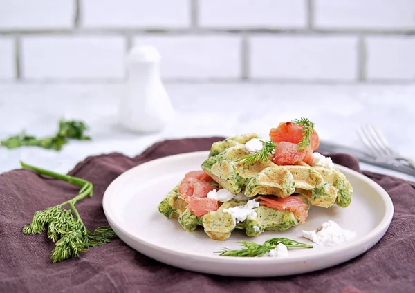 Light dinner, lunch or brunch, savory spinach snack waffles with salted salmon and cream cheese on a ceramic plate.