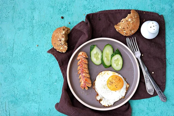 Kahvaltı, sosisli sahanda yumurta ve turkuaz beton arka planda kahverengi kil tabakta salatalık dilimleri. Çocuk kahvaltıları. Okul kahvaltı konsepti. Üst görünüm, alanı kopyala.