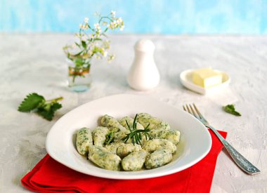 Gnocchi ya da ısırgan otlu börek ya da açık gri arka planda beyaz bir tabakta ıspanak. Tereyağı ve parmesan peyniri ile servis edilir. İtalyan yemeği. Seçici odak
