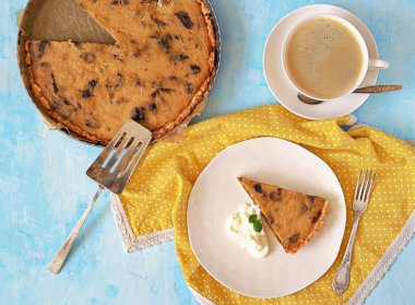 Açık mavi arka planda beyaz bir tabakta kuru erikli balkabağı turtası. Üst görünüm
