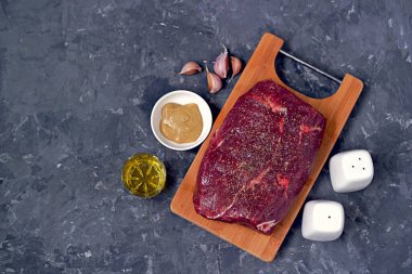 Biftek pişirmek için malzemeler: ahşap bir tahtada sığır eti, hardal, yağ, sarımsak, tuz, biber..