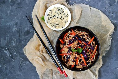 Buğday eriştesi, kırmızı lahana, havuç ve hindiyi siyah kasede kızartır. Siyah ve beyaz susam tohumlarıyla servis edilir. Çin yemeği. Üst görünüm, alanı kopyala.