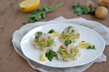 Beyaz ekmekli küçük sandviçler, guacamole ve beyaz tabakta karidesler. Seçici odak.