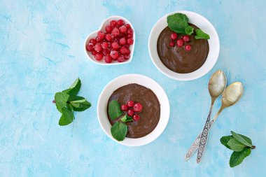 Tatlı tatlı, açık mavi arka planda beyaz tabakta çikolatalı puding. Nane ve kırmızı frenk üzümü ile süslenmiş. Sevgililer Günü konsepti. Üst görünüm.