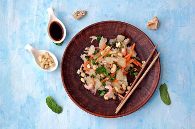 Açık mavi arka planda salata, karides, havuç ve fındık ezmesi. Asya mutfağı. Üst görünüm.