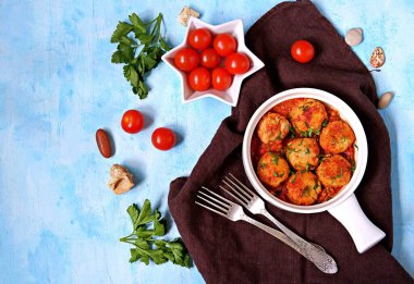 Açık mavi beton arka planda beyaz seramik tavada domates soslu balık köftesi. Üst görünüm, alanı kopyala.