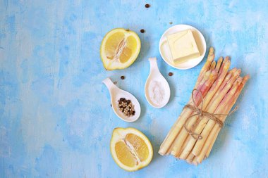Açık mavi beton arka planda kuşkonmaz pişirmek için gerekli malzemeler. Üst görünüm, alanı kopyala.