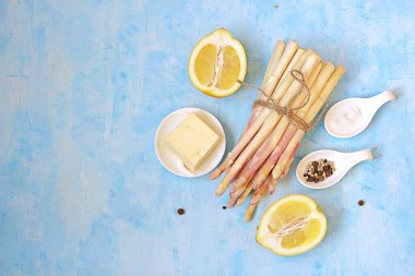 Açık mavi beton arka planda kuşkonmaz pişirmek için gerekli malzemeler. Üst görünüm, alanı kopyala.