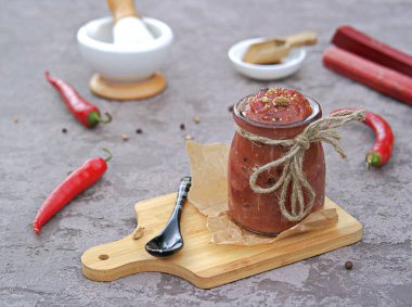 Gri arka planda cam bir kavanozda baharatlı ravent sosu. Korunuyor, hasat ediliyor. Hint yemeği..
