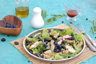 Arugula salatası, marul, ızgara tavuk ve turkuaz arka planda kahverengi bir tabakta hanımeli. Sağlıklı yiyecekler, diyet. Seçici odak