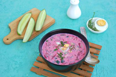 Yeşil soğanlı soğuk pancar çorbası, kefir soslu salatalık ve dereotu ya da turkuaz arka planda siyah bir kasede tereyağı. Haşlanmış yumurtayla servis edilir. Litvanya mutfağı. Sağlıklı yiyecekler, diyet. Boşluğu kopyala.