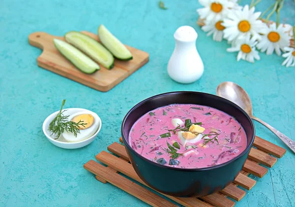 Cold beet soup with green onions, cucumber and dill on kefir or buttermilk in a black bowl on a turquoise background. Served with boiled egg. Lithuanian cuisine. Healthy food, diet. — Stock Image Cold Beet Soup Green Onions Cucumber Dill Kefir Buttermilk Black Stock Photo