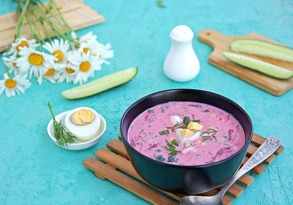 Cold beet soup with green onions, cucumber and dill on kefir or buttermilk in a black bowl on a turquoise background. Served with boiled egg. Lithuanian cuisine. Healthy food, diet. — Stock Image Cold Beet Soup Green Onions Cucumber Dill Kefir Buttermilk Black Royalty Free Stock Photos