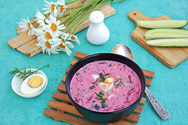 Cold beet soup with green onions, cucumber and dill on kefir or buttermilk in a black bowl on a turquoise background. Served with boiled egg. Lithuanian cuisine. Healthy food, diet. — Stock Image Cold Beet Soup Green Onions Cucumber Dill Kefir Buttermilk Black Royalty Free Stock Images