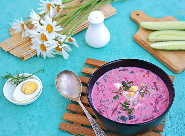 Cold beet soup with green onions, cucumber and dill on kefir or buttermilk in a black bowl on a turquoise background. Served with boiled egg. Lithuanian cuisine. Healthy food, diet. — Stock Image Cold Beet Soup Green Onions Cucumber Dill Kefir Buttermilk Black Stock Image