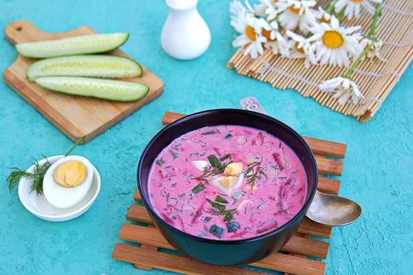 Cold beet soup with green onions, cucumber and dill on kefir or buttermilk in a black bowl on a turquoise background. Served with boiled egg. Lithuanian cuisine. Healthy food, diet. — Stock Image Cold Beet Soup Green Onions Cucumber Dill Kefir Buttermilk Black Royalty Free Stock Photos