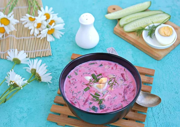 Cold beet soup with green onions, cucumber and dill on kefir or buttermilk in a black bowl on a turquoise background. Served with boiled egg. Lithuanian cuisine. Healthy food, diet. — Stock Image Cold Beet Soup Green Onions Cucumber Dill Kefir Buttermilk Black Stock Photo
