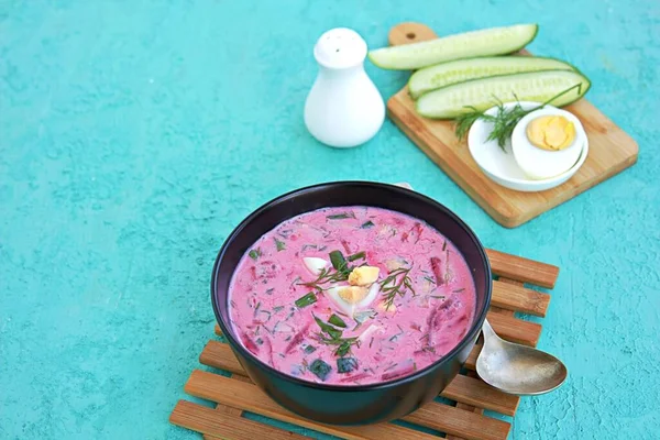 Cold beet soup with green onions, cucumber and dill on kefir or buttermilk in a black bowl on a turquoise background. Served with boiled egg. Lithuanian cuisine. Healthy food, diet. Copy space. — Stock Image Cold Beet Soup Green Onions Cucumber Dill Kefir Buttermilk Black Royalty Free Stock Photos