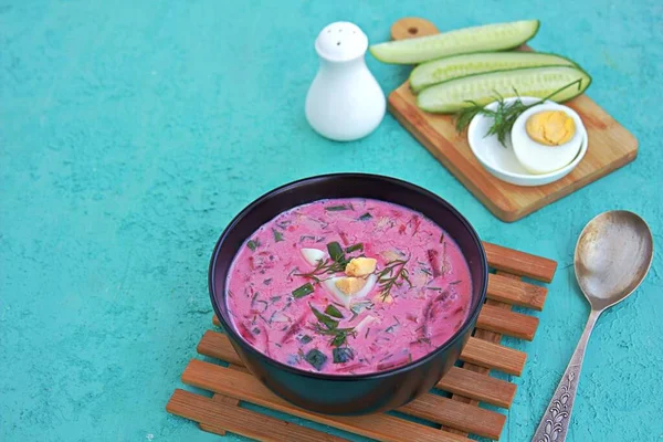 Cold beet soup with green onions, cucumber and dill on kefir or buttermilk in a black bowl on a turquoise background. Served with boiled egg. Lithuanian cuisine. Healthy food, diet. Copy space. — Stock Image Cold Beet Soup Green Onions Cucumber Dill Kefir Buttermilk Black Stock Image