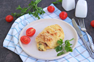 Ev yapımı Cordon Bleu filetosu ya da koyu kahverengi arka planda beyaz bir tabakta jambon ve peynirli tavuk filetosu. İsviçre mutfağı. Seçici odak.