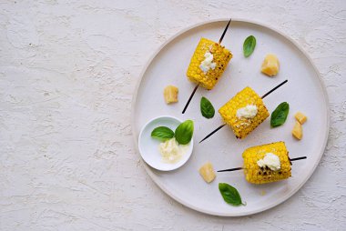 Beyaz seramik tepside ızgara mısır şişi. Tuzlu tereyağı ve rendelenmiş parmesan peyniri ile servis edilir. Sebze tabakları. Mısırları hasat et. Üst görünüm.