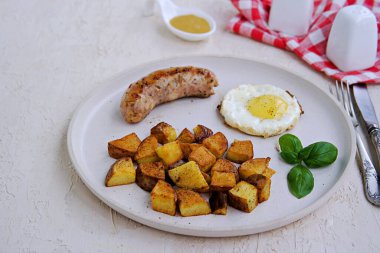 Büyük bir kahvaltı, patates kızartması, domuz sosisi ve hafif beton arka planda beyaz bir tabakta kızarmış yumurta. Amerikan yemekleri.