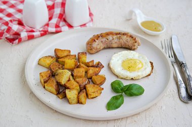 Büyük bir kahvaltı, patates kızartması, domuz sosisi ve hafif beton arka planda beyaz bir tabakta kızarmış yumurta. Amerikan yemekleri.