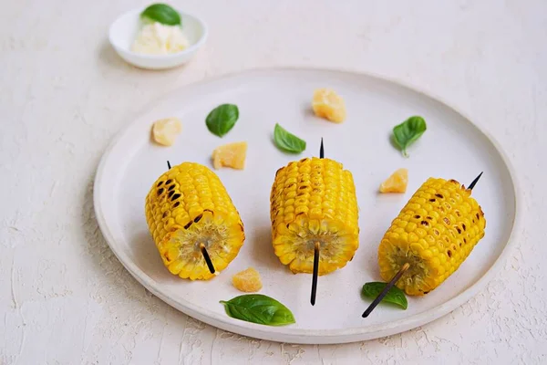 Beyaz seramik tepside ızgara mısır şişi. Tuzlu tereyağı ve rendelenmiş parmesan peyniri ile servis edilir. Sebze tabakları. Mısırları topla..