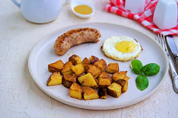 Büyük bir kahvaltı, patates kızartması, domuz sosisi ve hafif beton arka planda beyaz bir tabakta kızarmış yumurta. Amerikan yemekleri.