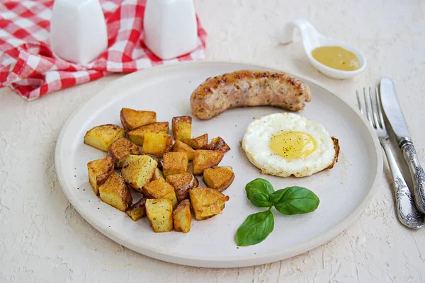 Büyük bir kahvaltı, patates kızartması, domuz sosisi ve hafif beton arka planda beyaz bir tabakta kızarmış yumurta. Amerikan yemekleri.