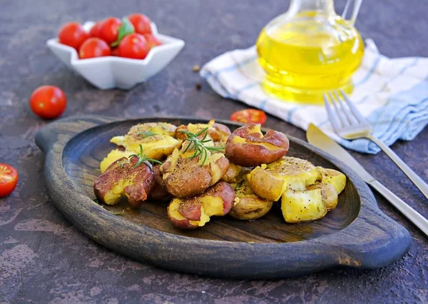 Crash Hot Potatoes, boiled potatoes in a peel, crushed and baked with olive oil and herbs on a wooden plate on a dark concrete background. Australian cuisine. Potato recipes. Thanksgiving Day