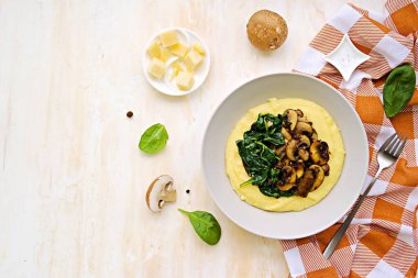 Bir porsiyon polenta ya da kızarmış mantarlı mısır ezmesi ve açık beton arka planda gri bir tabakta ıspanak. Polenta ya da mısır ezmesi tarifleri. İtalyan Mutfağı.