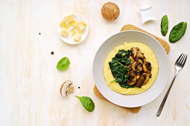 Bir porsiyon polenta ya da kızarmış mantarlı mısır ezmesi ve açık beton arka planda gri bir tabakta ıspanak. Polenta ya da mısır ezmesi tarifleri. İtalyan Mutfağı.
