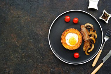 Kızarmış mantar, domuz pastırması ve domatesli balkabağı halkası içinde sahanda yumurta, koyu beton bir arka planda. Balkabağı tarifleri. Şükran Günü.