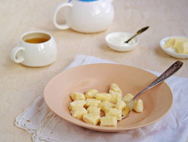 Hafif beton arka planda kil bir tabakta süzme peynirden yapılan tembel hamur tatlısı ya da gnocchi. Ekşi krema ve tereyağlı. Süzme peynirden tabaklar. Sağlıklı kahvaltı. Seçici odak.