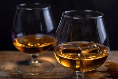 Ahşap zemin üzerinde buz olan iki viski ve konyak bardağı. Karanlık arkaplan.