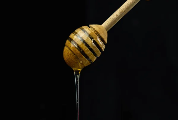 Liquid honey on a special wooden stick spoon on a black background
