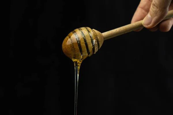 Liquid honey on a special wooden stick spoon on a black background