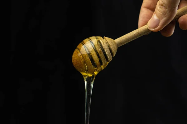 Liquid honey on a special wooden stick spoon on a black background