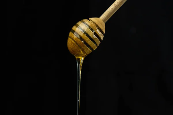 黒の背景に特別な木の棒スプーンで液体蜂蜜 — ストック写真