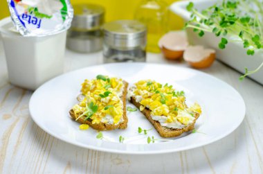 Feta peynirli sağlıklı tam buğday ekmeği, çırpılmış yumurta ve mikroyeşillikler, kahvaltıda uygun beslenme sandviçleri.