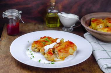 Havuçlu ev yapımı lahana ruloları, beyaz tabakta kırmızı domates sosu ve krema.