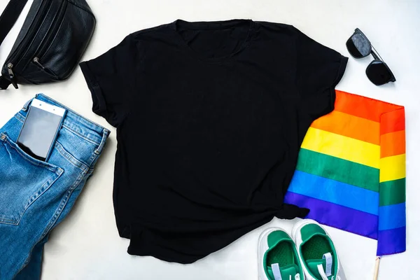 black t-shirt mockup for print. Flatlay with gay pride flag and casual clothes. Blue jeans, black sunglasses, white sneakers and shoulder bag