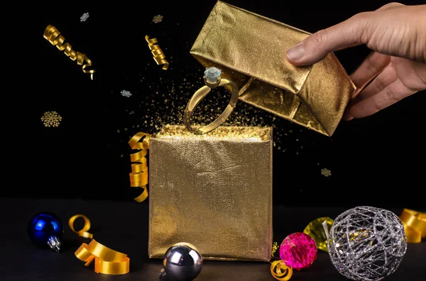 Open Magic Christmas Gift Box with presents, decoration, golden dust, particles, ribbon and gold diamond ring. New Year gifts