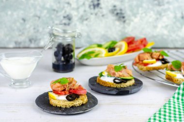 Hafif ahşap zemin üzerinde pembe somon balığı, salatalık, domates, zeytin ve limon bulunan küçük bir kanepe.